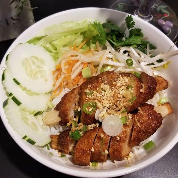 A Vietnamese dish with crispy pork, rice noodles, fresh vegetables, and peanuts in a white bowl.