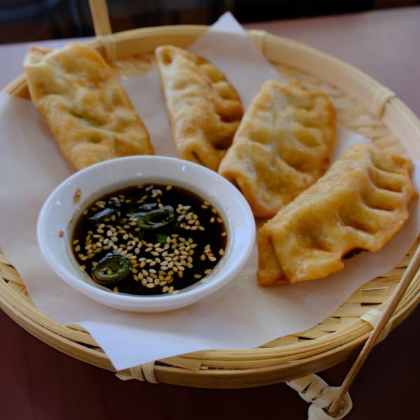 Four golden-fried Vietnamese dumplings with a side of soy sauce, sesame seeds, and jalapeños.