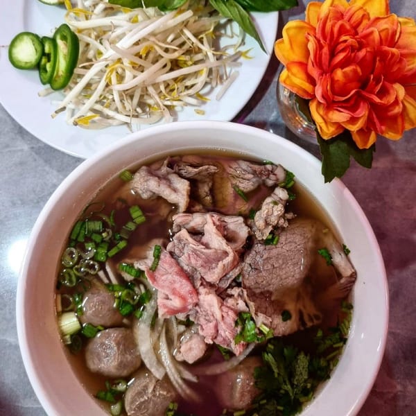 A bowl of Pho Akaushi beef pho with a side of bean sprouts, jalapeños, and basil.