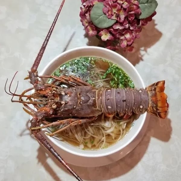 A whole cooked lobster rests atop a bowl of Vietnamese pho noodles and broth.
