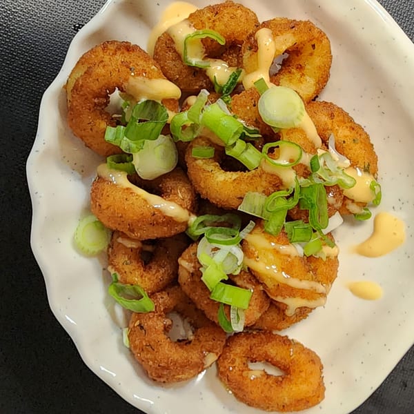 Crispy fried calamari rings drizzled with creamy sauce and garnished with fresh green onions.