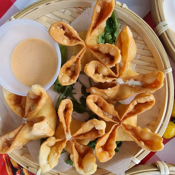 Crispy crab rangoon appetizers with a side of dipping sauce on a bamboo tray.