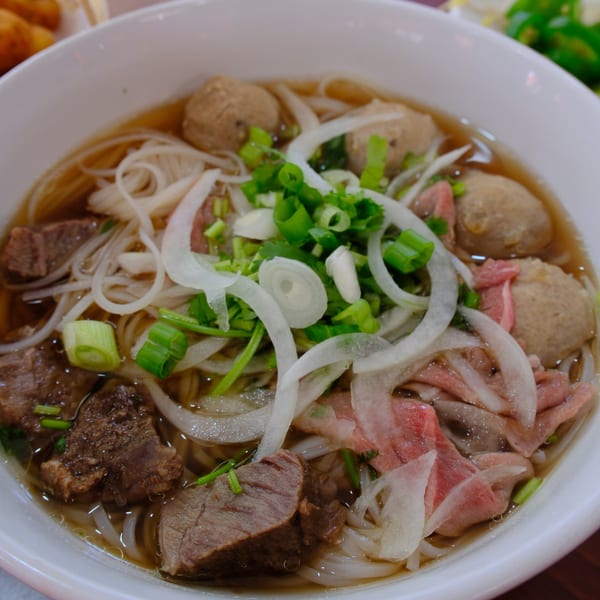 Close-up of a bowl of Pho Akaushi pho with beef, meatballs, noodles, onions, and scallions.