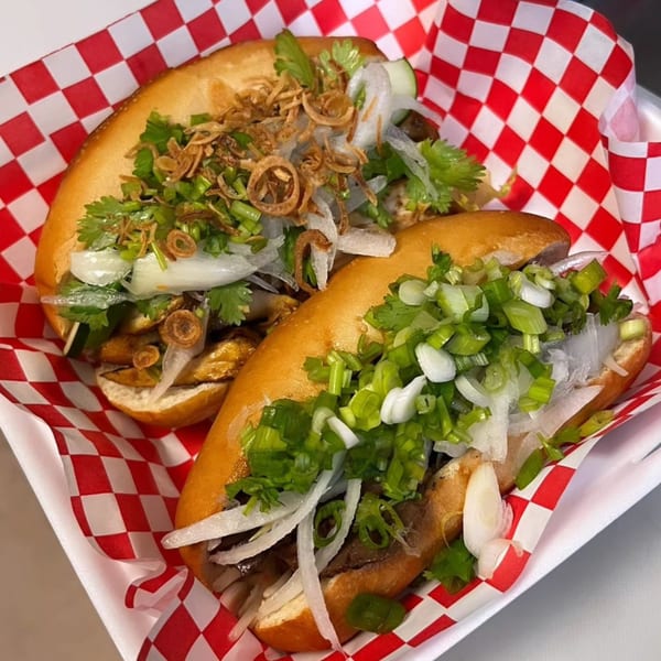 Two Vietnamese banh mi sandwiches with various toppings in a red and white checkered paper-lined basket.