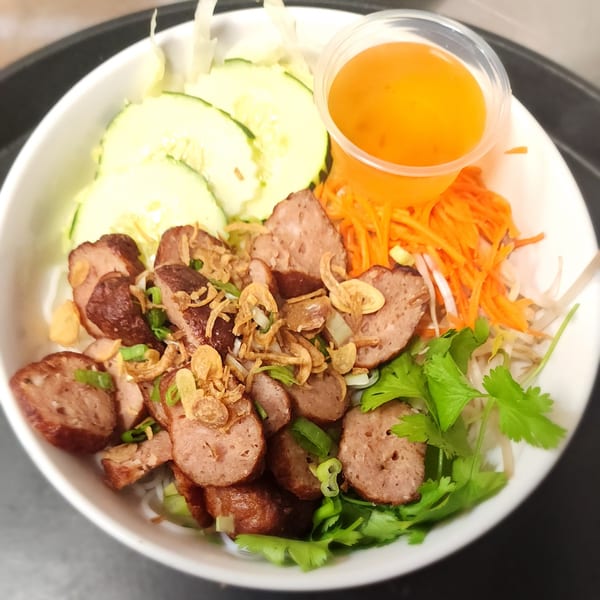 Vietnamese vermicelli bowl with sliced sausage, fresh cucumbers, shredded carrots, cilantro, and sauce.